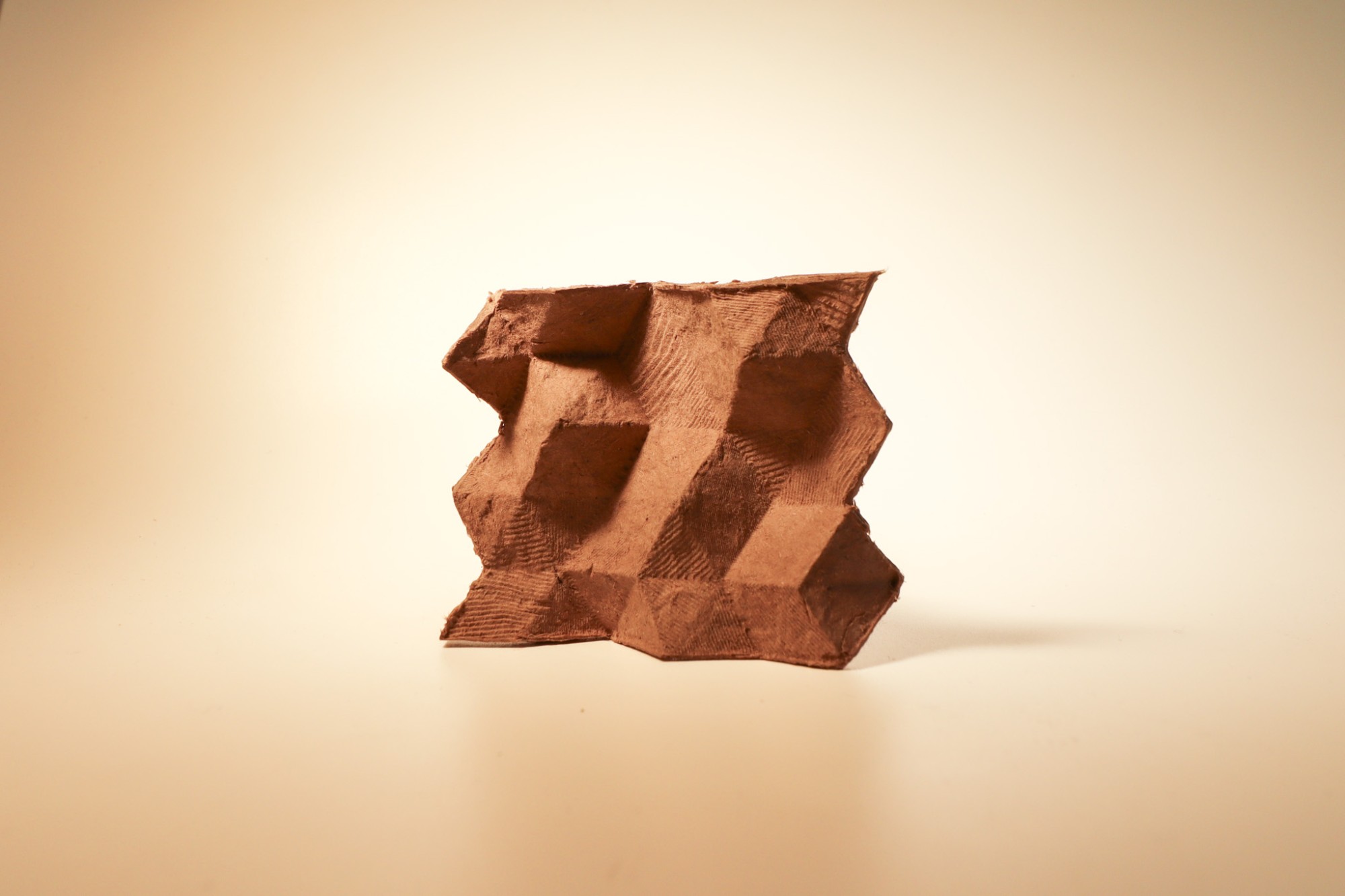 A molded cardboard-pulp prototype with a geometric, faceted surface