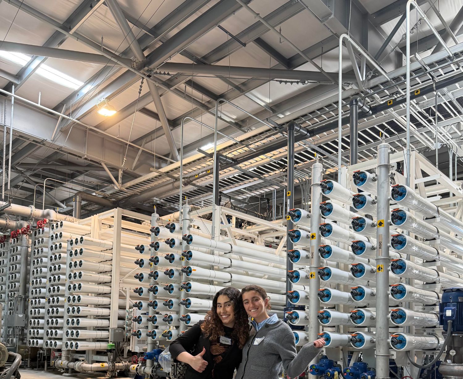 Two smiling visitors in front of towering racks of white reverse osmosis pressure vessels at the Albert Robles Center for Water Recycling & Environmental Learning