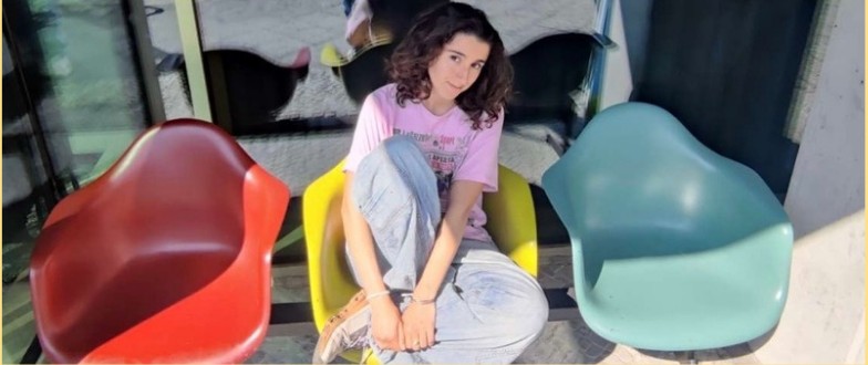 Leilani sitting between three mid-century modern chairs in red, yellow, and mint