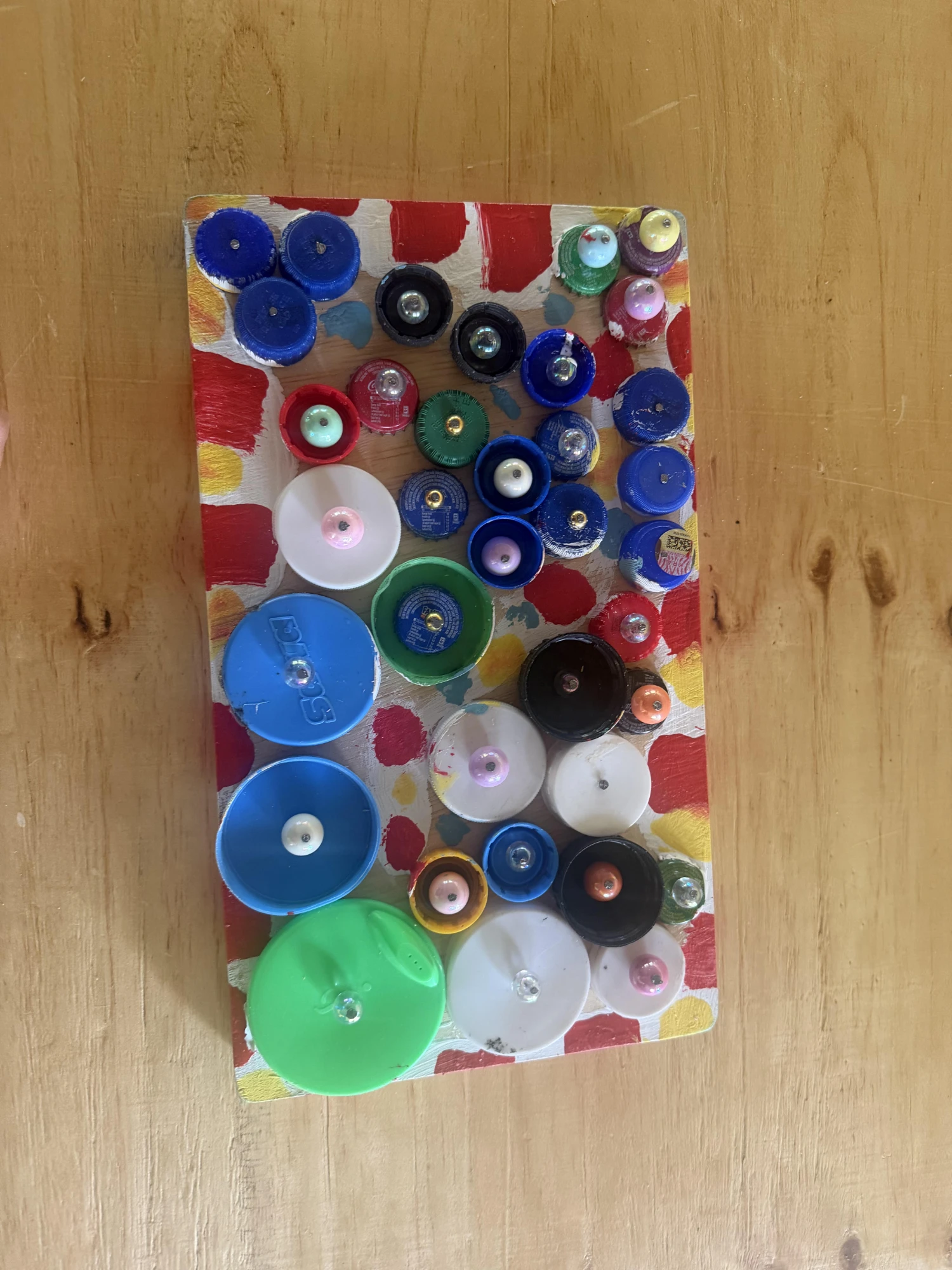 Fine motor fidget board: dozens of recycled plastic bottle caps with beads at their centers, fixed to a board painted with red and yellow dots