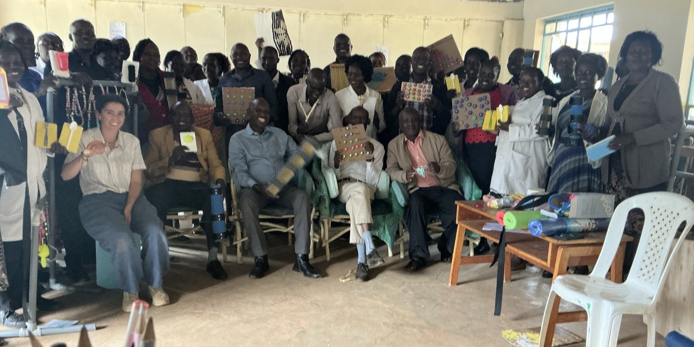 Leilani with the teachers and school leaders of Kabarnet School for the DeafBlind, holding up the cue cards, spoon handles, counting boards and braces they built in the workshop