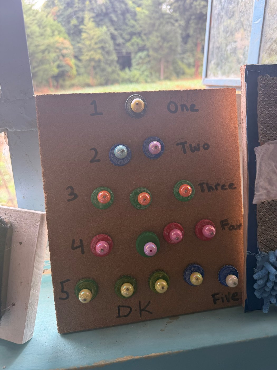 A cork counting board with the numbers one to five, each row holding that many bottle caps topped with beads to touch and count