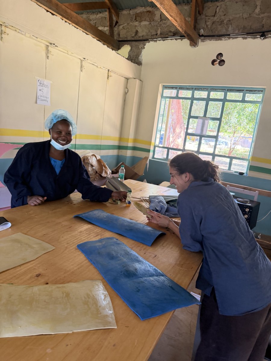 Leilani and a smiling woman in a hairnet and navy work coat at a workbench laid out with flattened blue PVC sheets and foam lining