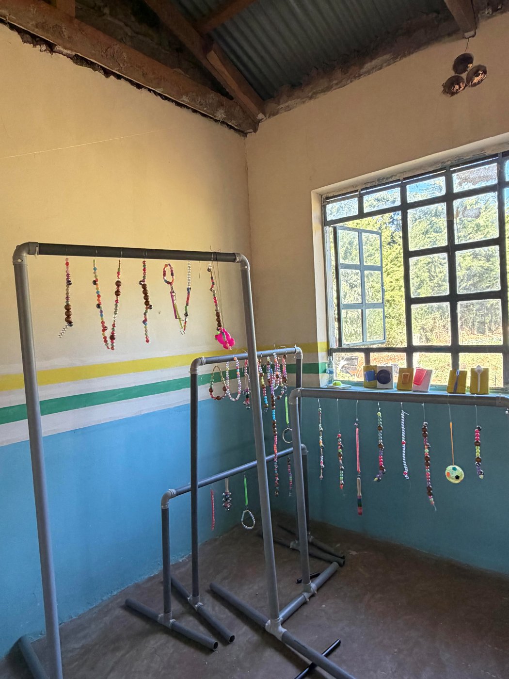 Three PVC-pipe sensory curtain frames in the workshop, hung with strands of colorful beads, rings and a small ball