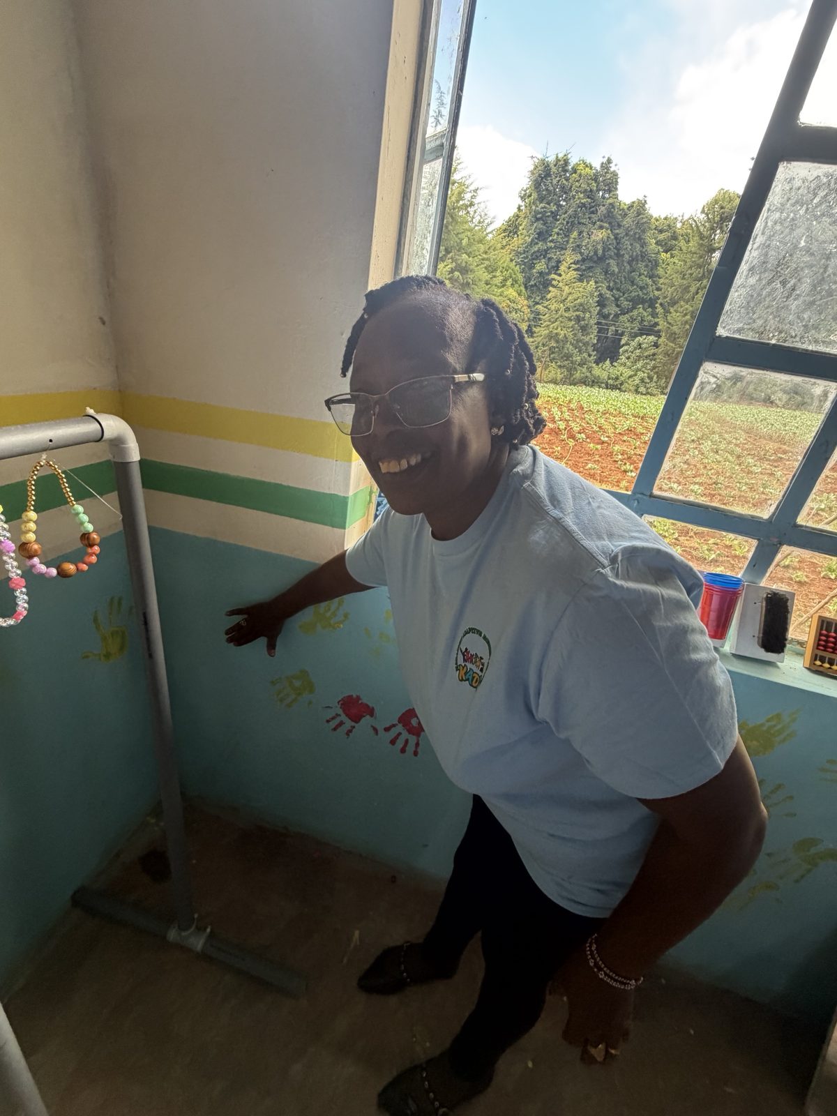 A smiling teacher in glasses pressing her hand onto the wall beside a PVC sensory curtain hung with beads