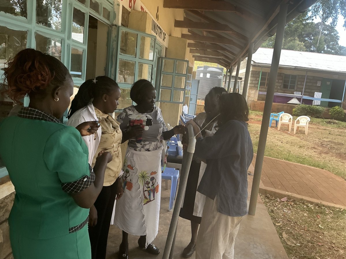 Leilani and a group of teachers on the veranda outside the workshop, threading strands onto an upright PVC pipe frame with a drill in hand