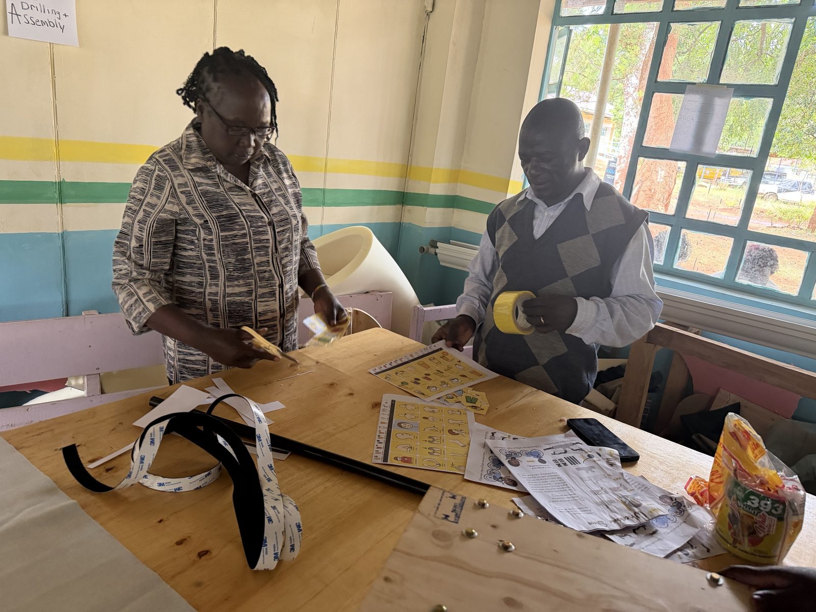 Two teachers at a workshop table cutting out yellow picture symbol cards and strips of hook-and-loop tape for a communication board