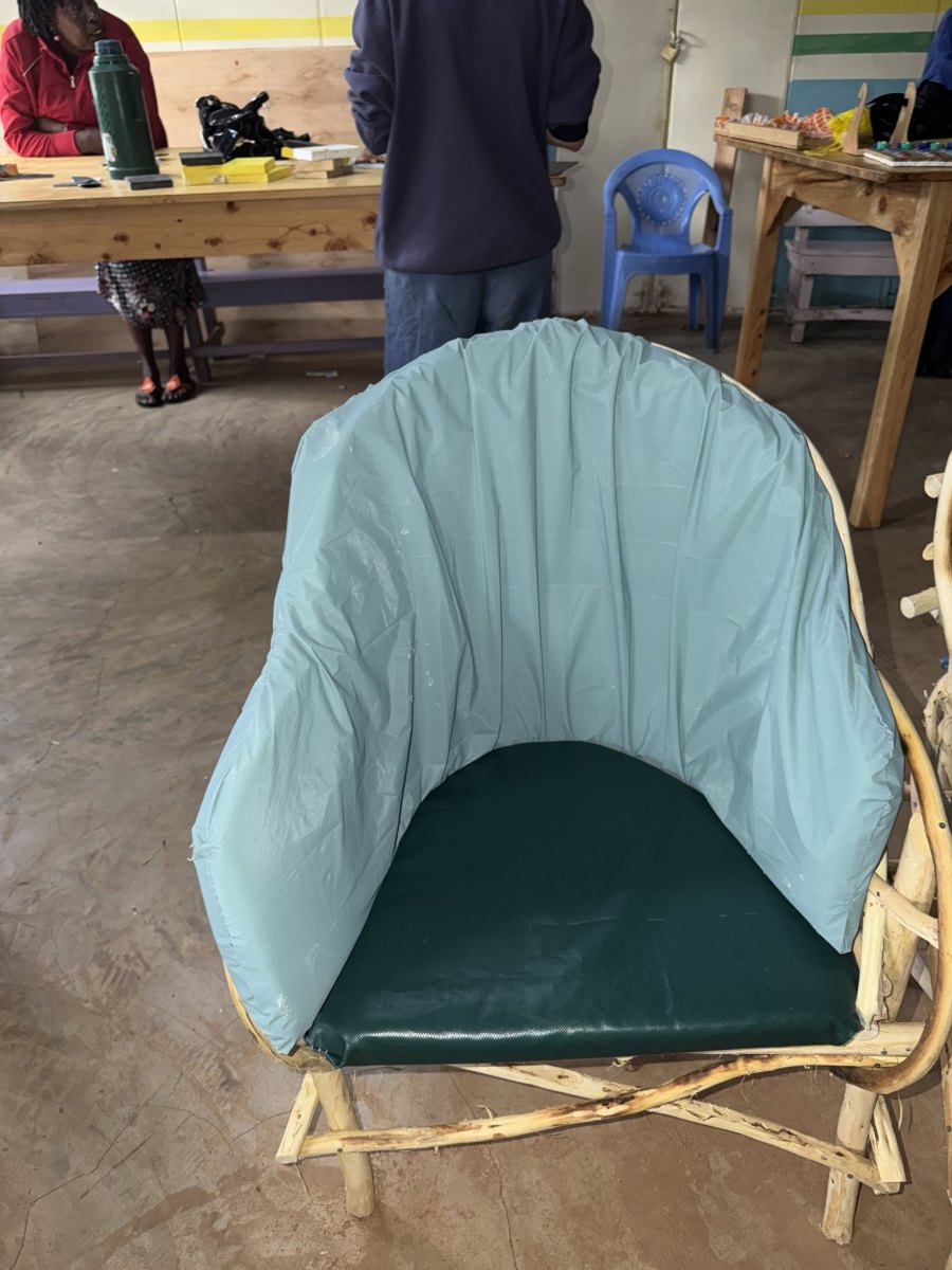 A finished chair built from peeled cypress branches, with a padded light blue backrest that wraps around the sides and a dark green seat cushion