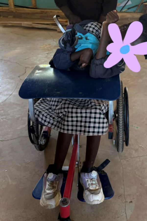 Before fitting: a learner slumped forward over the tray of an ill-fitting wheelchair, without support to sit upright; her face is covered for privacy