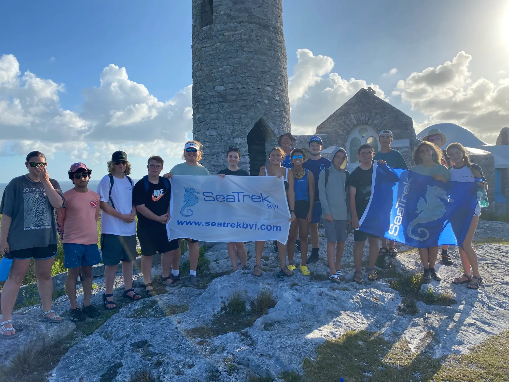 Seatrek students holding Seatrek banners in front of a stone tower on a rocky hilltop