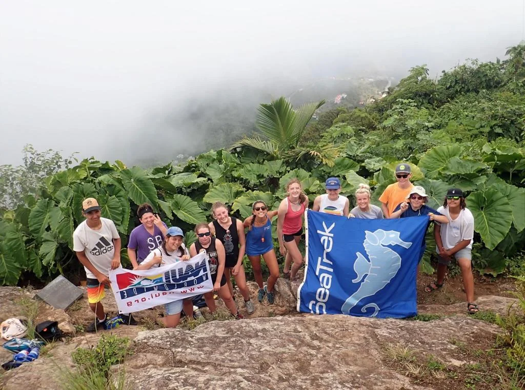 Students with a Seatrek flag on a misty, jungle-covered summit