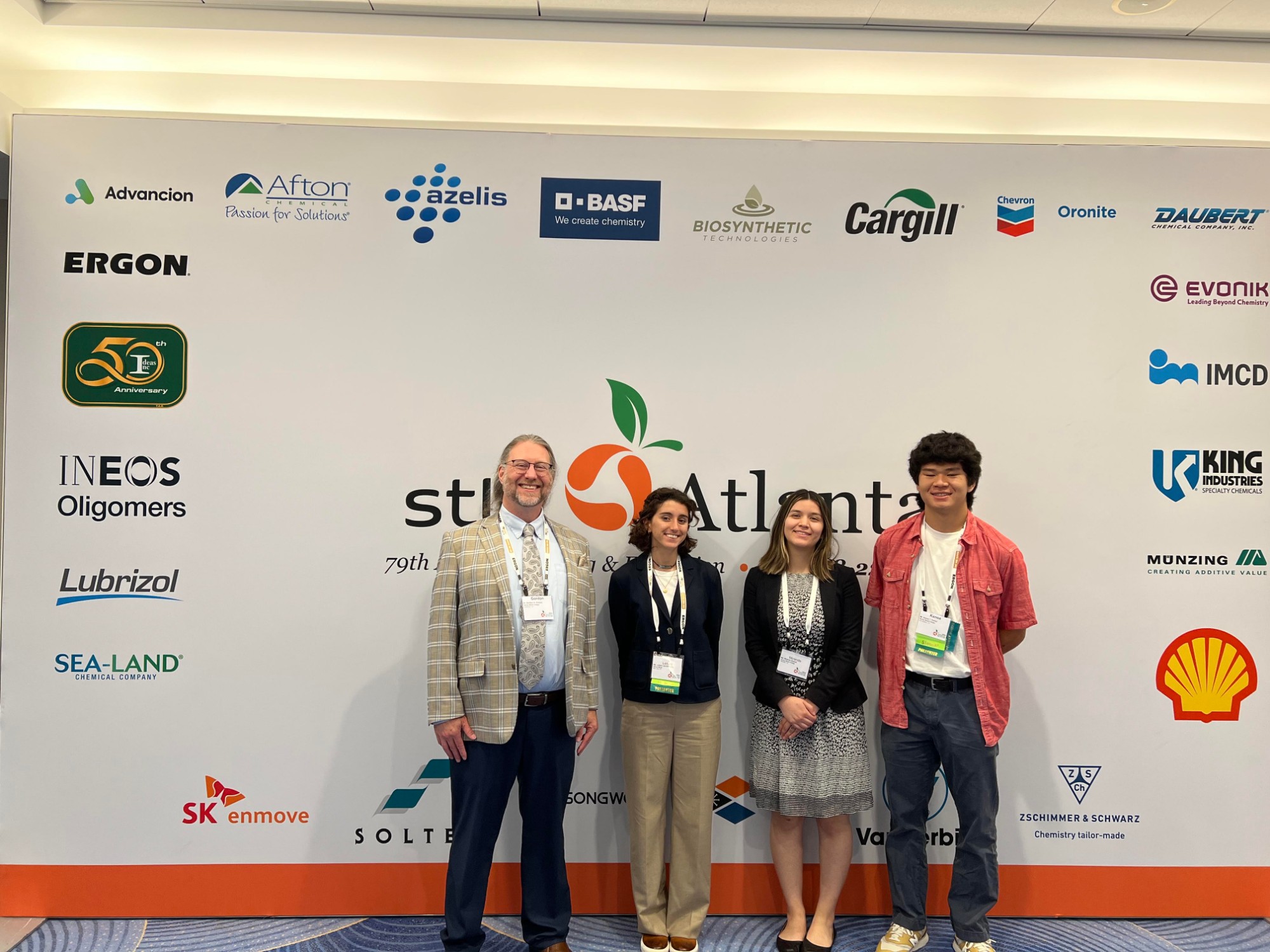 Four team members standing in front of the STLE Atlanta sponsor wall at the conference